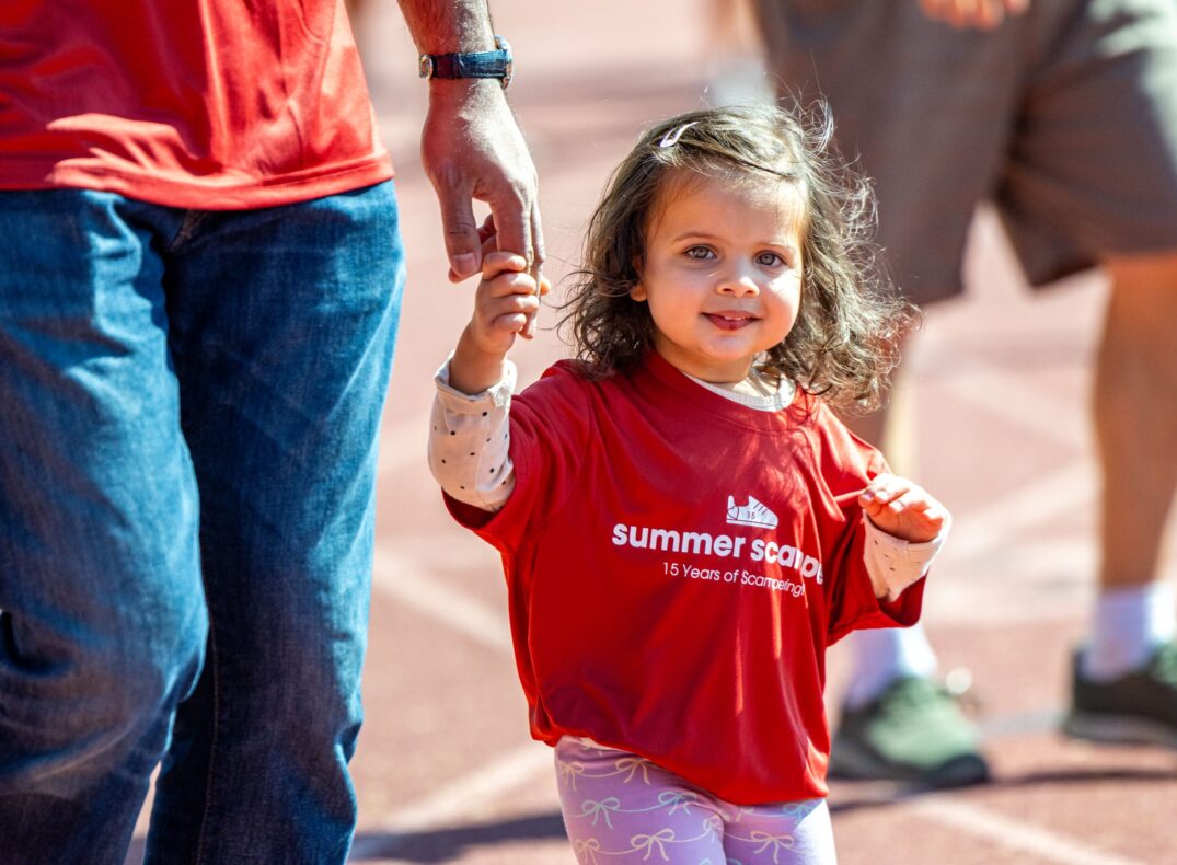 A little girl holds an adult's hand as she walks on the track.