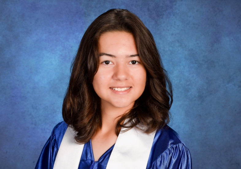 A high school graduate looking directly at the camera with a bright, welcoming, and genuine smile. They wear a satin blue graduation gown and white stole against a clean, well-lit background.